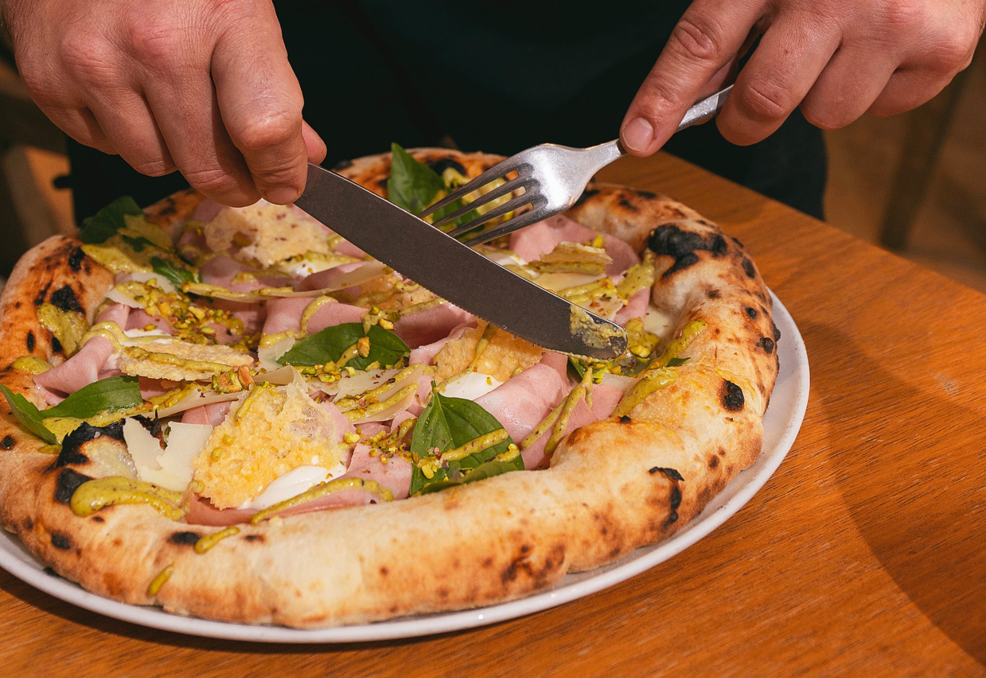 Pizza de Atrezzo con mortadela, albahaca y queso, cortándose a la mesa